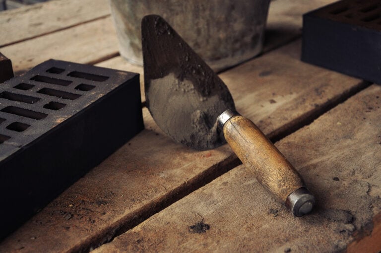 Masonry tools on a wooden board including trowels, hammers, chisels, and a level.